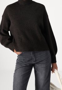 Tummanruskea neulottu pusero, jossa korkea resorinen kaulus, yläkoon malli ja resorinen helma, yhdistetty harmaisiin farkkuihin.