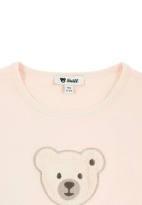 Camiseta de algodón de color rosa claro con un aplique texturizado de cara de oso en blanco y gris, con cuello redondo y dobladillo cosido. Etiqueta visible.