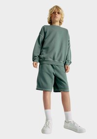 Grøn bomulds sweatshirt og matchende shorts, der har ribbede manchetter og kant. Sammen med hvide sneakers og ribbede hvide sokker.