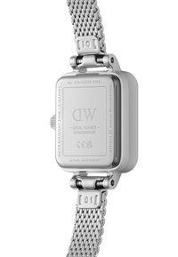Montre en acier inoxydable avec un bracelet en maille, boîtier rectangulaire et détails gravés au dos, incluant la marque et le numéro de série.
