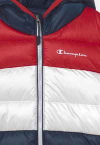 Padded bunda v červené, bílé a námořnické modré barvě se zipem vpředu. Na hrudi se nachází logo Champion a má podšitou kapuci pro zajištění větší tepla.