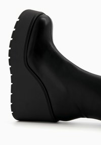 Bota cuña negra con parte superior de cuero liso, suela plataforma gruesa y suela exterior texturizada con ranuras prominentes.