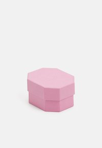 Rozā sešstūru kaste, izgatavota no teksturēta materiāla, ar platu vāku, kurā ir iegriezts apļa logotips, un stabilu pamatni.