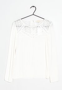 Blusa bianca a maniche lunghe con un pannello in pizzo trasparente all'collo e tessuto testurizzato. Orlo arrotondato e chiusura a gancio sul retro.