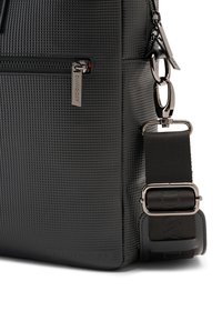 Black textured bag with a zippered pocket, featuring silver hardware and an adjustable strap with a buckle, embossed brand logo on the side.