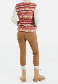 Miękki, pasiasty bezrękawnik w ciepłych odcieniach z niebieskim, zestawiony z brązowymi, dopasowanymi spodniami oraz beżowymi sznurowanymi butami z fakturowaną podeszwą.