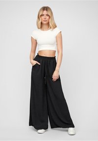 Black wide-leg trousers with an elastic waistband and drawstring, made of soft fabric. Paired with a fitted white cropped T-shirt.