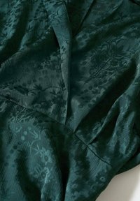 Tissu vert foncé avec un motif jacquard floral subtil et des plis doux, mettant en valeur la texture et le tombé.