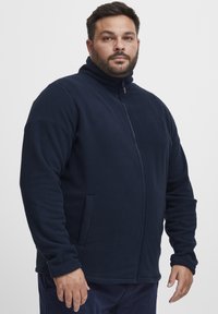 Chaqueta de forro polar navy con cuello alto, cremallera completa y bolsillos laterales. Cuenta con una textura suave y un diseño clásico, adecuado para uso casual.