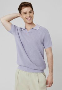Polo en maille violette claire à manches courtes avec un col en V et un ourlet côtelé. Associe à un pantalon de couleur claire.