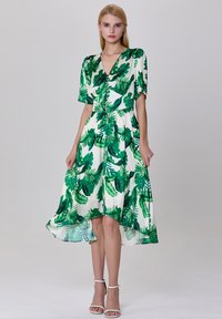 Robe à motif de feuilles vertes avec des manches courtes, décolleté en V, détail de boutons et un ourlet fluide. Fabriquée en tissu léger et lisse.