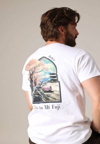 T-shirt en coton blanc avec une illustration colorée d'une voiture rose, de cerisiers en fleurs et du Mont Fuji, avec le texte "Deluxe" en haut.