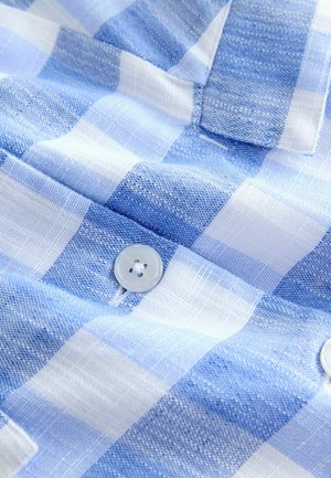 Tessuto a quadretti blu e bianco con un primo piano di un bottone bianco cucito su una camicia dalla texture evidenziata.