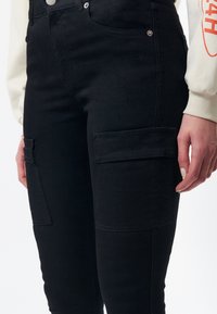 Pantalones cargo negros de denim con bolsillos laterales, cintura alta y detalles de costura sutiles cerca de los bolsillos.