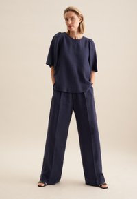Top in lino blu navy con maniche corte e scollatura rotonda, abbinato a pantaloni larghi in lino blu navy. Tessuto liscio con dettagli minimi.