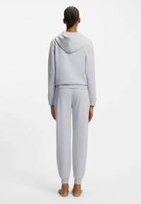 Harmaa huppari ja siihen sopivat pehmeästä kankaasta tehdyt collegehousut. Hupullinen malli, jossa resorit hihansuissa ja vyötäröllä. Rentoa istuvuutta kaventuvilla lahkeilla.