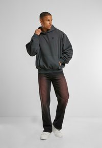 Kuld hoodie med en kængurulomme, afslappet pasform og ribbede manchetter. I kombination med mørke jeans med en falmet gradient effekt og hvide sneakers.