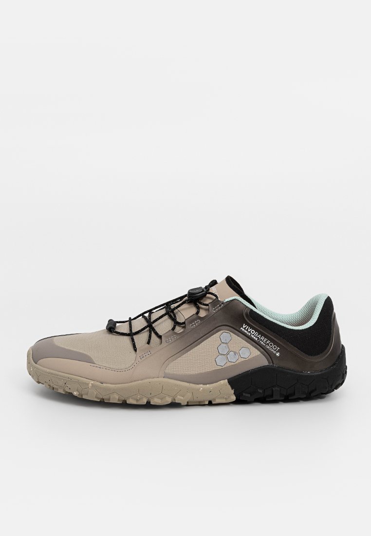 Zapatilla de trail running Vivobarefoot en beige y negro, con logo hexagonal, sistema de cordones rápido y suela texturada para uso en exteriores.