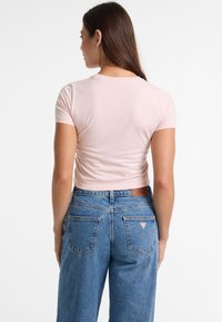 Pink cropped t-shirt with short sleeves, paired with high-waisted blue denim jeans. Distinctive logo on back pocket, smooth, fitted fabric.