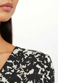 Tessuto a motivo bianco e nero con una texture liscia, caratterizzato da un profondo scollo a V e dettagli strutturati delle spalle leggermente morbidi.