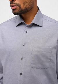 Hemd mit Knopfleiste in Grau und Schwarz mit kleinem Karomuster, ausgestattet mit einem spitzen Kragen, einer Brusttasche und drei sichtbaren Knöpfen an der Knopfleiste.