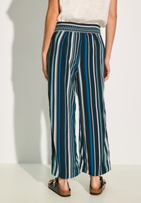 Spodnie o szerokich nogawkach w pionowe paski w odcieniach niebieskiego, granatowego i białego, z gumką w pasie i gładkiego, lekkiego materiału.