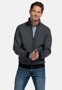 Graue Zip-Jacke mit strukturierter Oberfläche, schwarzen gerippten B�ündchen und Saum sowie einer Brusttasche. Getragen über einem blauen gemusterten Hemd.