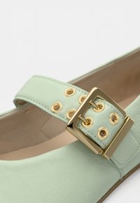 Πράσινο μέντας δερμάτινο παπούτσι με φαρδιά λουρίδα που διαθέτει χρυσή αγκράφα και μεταλλικά ροδέλες, λεία υφή και στρογγυλεμένο σχέδιο μύτης.