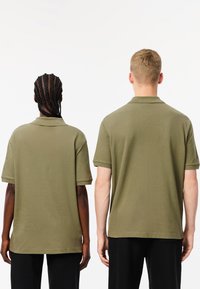 Två individer som bär olivgröna polo t-shirts med korta ärmar. T-shirtarna har en klassisk krage och en avslappnad passform.