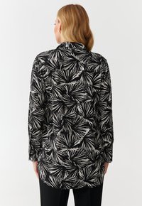 Camicia a maniche lunghe in bianco e nero con un motivo a foglie, con taglio dritto, colletto a bottoni e texture liscia.