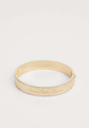 Gouden armband met de gegraveerde tekst "Lauren Ralph Lauren" en een rij kleine heldere stenen langs de rand. Gladde oppervlakte, slank ontwerp.