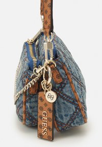 Džínov�á kabelka se zlatými prvky, hnědými logovými akcenty a prošívanou strukturou. Obsahuje dvojité zipy a odnímatelný řetízek.