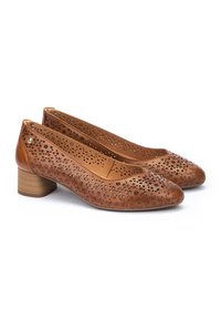 Ballerines en cuir tan avec des motifs floraux perforés, bout rond et petit talon bloc. L'intérieur est d'une couleur tan uni.