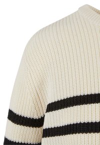 Maglione lavorato a maglia color crema con strisce orizzontali nere. Presenta un tessuto testurizzato e un collo rotondo. Primo piano della zona della spalla.