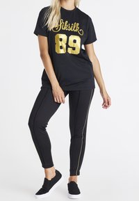 Černé tričko s zlatým potiskem "SikSilk" a číslem "89"; spárované s černými slim-fit kalhotami se zlatými bočními pruhy a černými nazouvacími botami.