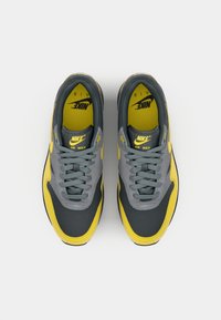 Nike Air Max sneakers featuring a gray upper with yellow accents, mesh texture, round laces, and prominent branding on the tongue.