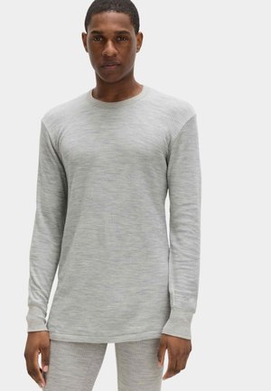 Hombre con camiseta de manga larga acanalada de color gris claro y pantalones a juego, de pie frente a un fondo blanco liso.