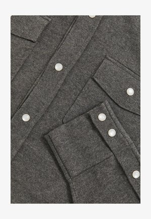 Tejido de punto gris oscuro con botones a presión, bolsillos en el pecho y un puño con dos botones a presión, mostrando un primer plano de una prenda.