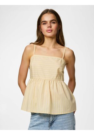 Jonge vrouw draagt een geel mouwloos topje met dunne bandjes en subtiele verticale strepen, gecombineerd met lichtblauwe spijkerbroeken.