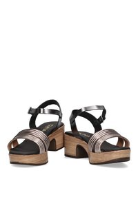 Sandalias de tiras en negro y bronce con un tacón de bloque con textura de madera y una banda media metálica ancha y estriada. Correa en el tobillo ajustable para un mejor ajuste.