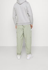 Grå hoodie med kenguruficka, parat med ljusgröna cargobyxor med sidofickor, elastiska mudd och vita sneakers.