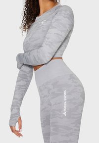 Woman wearing matching grey camouflage seamless long-sleeve crop top and high-waisted leggings with thumb holes and "SQUATPROOF" branding.