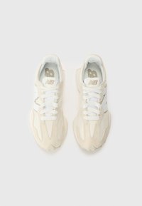 Paire de baskets New Balance beige et blanches avec lacets, vues du dessus sur un fond clair uni.