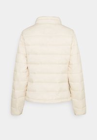 Kremowa pikowana kurtka z poziomym przeszyciem widoczna z tyłu, z długimi rękawami i stojącym kołnierzem.