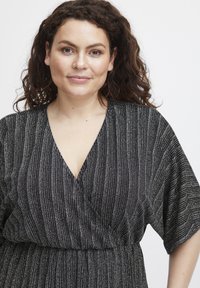 Svart omlottklänning med silverrandigt mönster, djup V-ringning, korta fladderärmar, midja som är insydd och mjuk tygtextur.