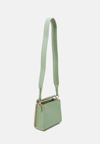 Piccola borsa a tracolla in pelle verde chiaro con lungo cinturino regolabile e dettaglio laterale intrecciato color nocciola, mostrata su sfondo bianco.