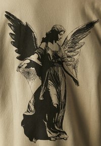 Beiger Stoff mit einer schwarzen Grafik einer engelhaften Figur. Die Figur hat ausgebreitete Flügel, ein fließendes Gewand und Spinnennetzakzente.