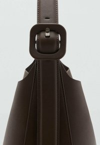 Brown leather handbag featuring a structured design, flat base, and a rectangular buckle on the strap with contrasting stitching details.