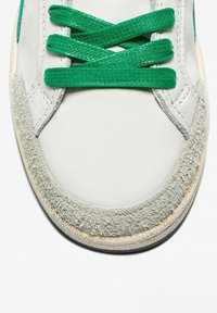 Sneaker bianco con lacci e dettagli verdi, con una punta in suede grigio testurizzato e una tomaia in pelle liscia.