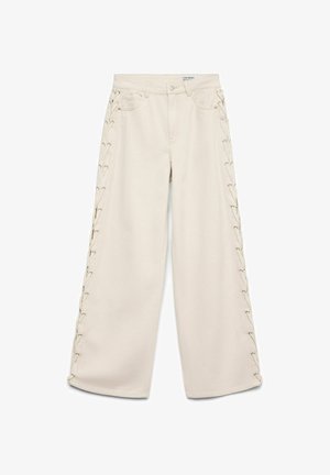 Pantalon beige à jambes larges avec des détails à lacets courant verticalement le long des deux côtés extérieurs et un design classique à cinq poches.